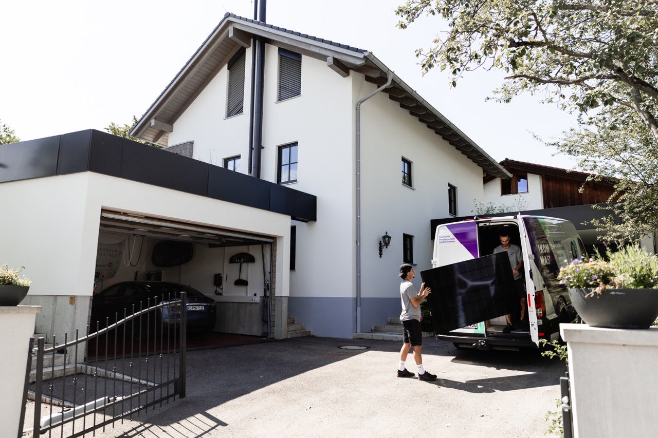 Montörer från 1KOMMA5° bär ut solcellspanel från bil på en garageuppfart till en villa i Örebro